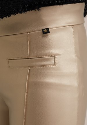 Faux leather beige pants feature a smooth texture, a back pocket with stitching, and a small black tag with a gold star accent.