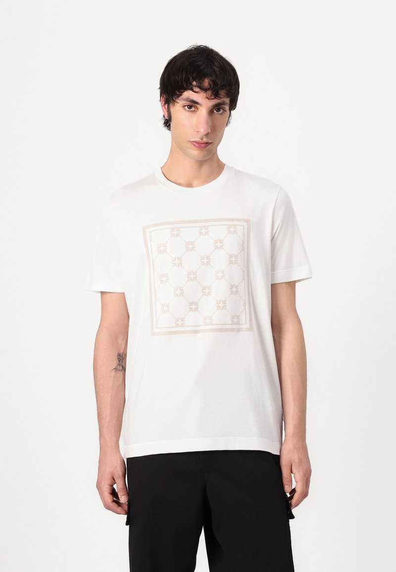 Camiseta blanca de algodón con un gráfico cuadrado que presenta un patrón floral repetido en tonos beiges. Mangas cortas y escote redondo.
