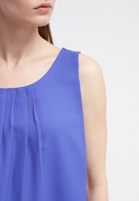 Hihaton violetti yläosa pyöreällä pääntiellä, jossa pystysuuntaiset laskokset edessä, valmistettu sileästä, kevyestä kankaasta.