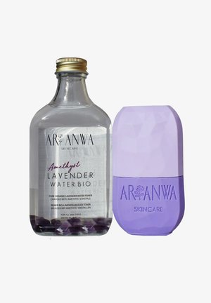 Bouteille en verre clair avec un capuchon doré, étiquetée "Eau de lavande améthyste Bio" contenant des cristaux violets. Bouteille applicatrice en plastique violet avec un design texturé.