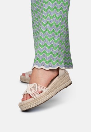Sandalias de espadrille con parte superior de un marrón claro tejido, suela de cuña envuelta en yute y un patrón texturizado en pantalones suaves en tonos pastel verde y gris.
