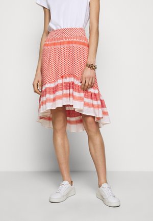 Roter gemusterter Rock mit einem hohen und niedrigen Saum, ausgestattet mit einem strukturierten Bund und geschichteten Rüschen. Kombiniert mit weißen Sneakers für einen Kontrast.