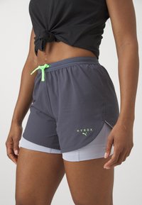 Grå treningsshorts med en neongrønn snor, med et innerlag og "HYROX"-logo. Jevn tekstur, design som går til midt på låret.