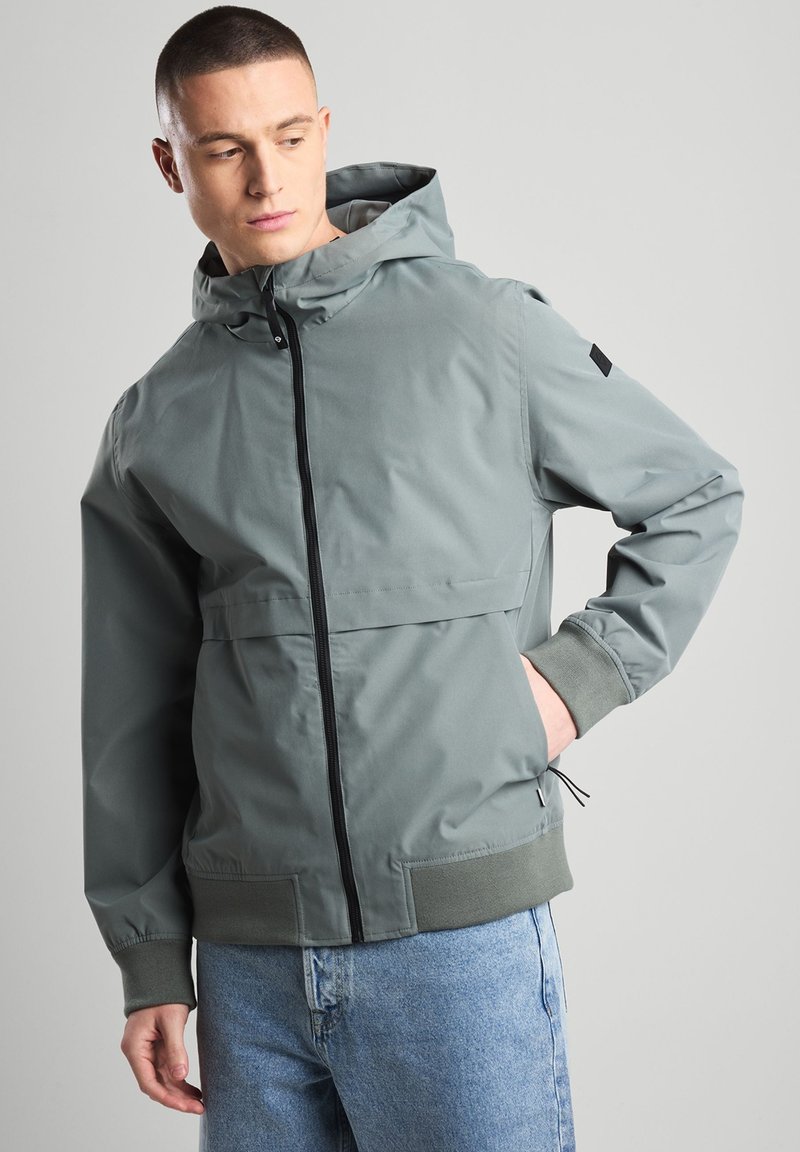 Hooded jacket in grey, featuring a front zipper, elastic cuffs, and a relaxed fit. The material has a smooth finish with a matte texture.