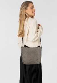 Borsa a spalla in pelle grigia con una texture liscia, chiusura con zip e tracolla regolabile, caratterizzata da un design minimalista e angoli arrotondati.