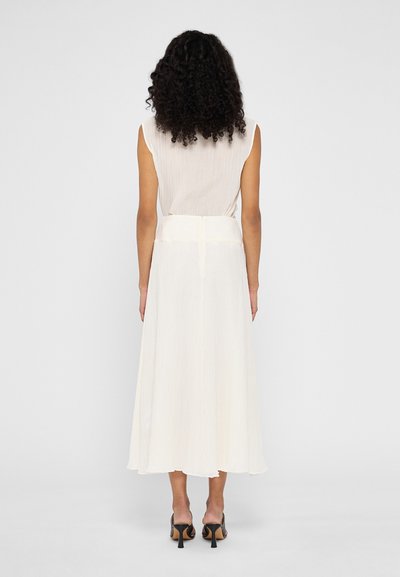 Robe de couleur crème clair avec un design évasé et plissé. Sans manches, avec une taille cintrée et un tissu fluide, atteignant le mi-mollet.