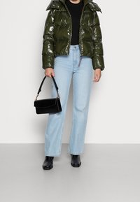 Skinny mørkegrøn pufferjakke med hætte, sort top, lyseblå lige ben jeans og sort håndtaske. Sorte ankelstøvler fuldender looket.