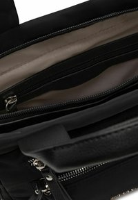 Borsa nera con una superficie testurizzata, dotata di chiusura con zip e scomparti interni foderati in morbido beige.