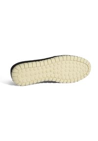 Zwarte sneaker zool met een gestructureerde crèmekleurige rubberen zool, voorzien van ronde grip en een patroonontwerp, dat zorgt voor grip en stabiliteit.