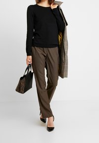 Zwart top met lange mouwen gecombineerd met bruine broek, een geruite jas en een zwarte handtas met slangenmotief. Het model draagt zwarte hakken.