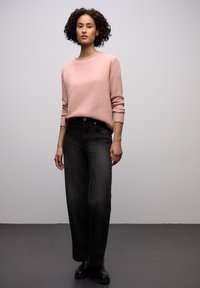 Světlounce růžový svetr s kulatým výstřihem ve spojení s černými širokými kalhotami s vysokým pasem. Modelka má na nohou černé kotníkové boty. Jednoduchý, čistý design.