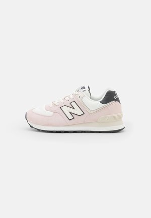 Lyserød og hvid New Balance-sneaker med sort "N" logo, hvide snørebånd og sort hæl-detalje på hvid baggrund.