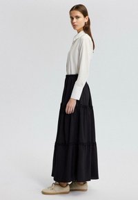 Witte lange mouwen blouse met kraag, gecombineerd met een zwarte gelaagde maxi rok met ruches, afgemaakt met beige sneakers.