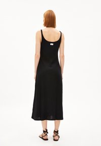 Black ribbed midi dress with a scoop back, adjustable straps, and a tag on the upper back. Footwear features strappy black sandals.