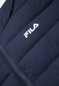 Marinblå pufferväst i slät tyg, med quiltade sektioner och central dragkedja. Märkt med en vit "FILA"-logotyp.