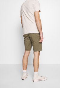 T-shirt di cotone beige chiaro, pantaloni corti verde oliva, scarpe sportive, calzini bianchi alla caviglia. Pantaloni corti con risvolto, vestibilità casual. Vista posteriore dell'outfit presentato.