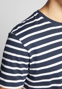 Marineblå og hvide stribet T-shirt med rund halsudskæring og korte ærmer; stoffet ser glat ud med en let glans. Ingen synlige logoer.