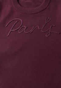 Pull en tricot bordeaux avec le mot "Party" brodé en fil assorti sur la poitrine en lettres cursives.