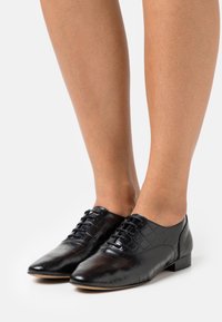 Chaussures en cuir noir avec un motif crocodile, dotées d'un petit talon et d'un laçage sur le devant. Texture lisse et design à bout pointu.