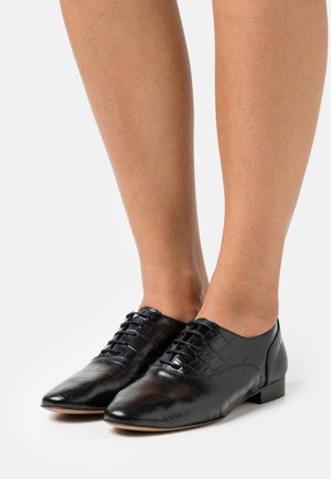 Chaussures en cuir noir avec un motif crocodile, dotées d'un petit talon et d'un laçage sur le devant. Texture lisse et design à bout pointu.