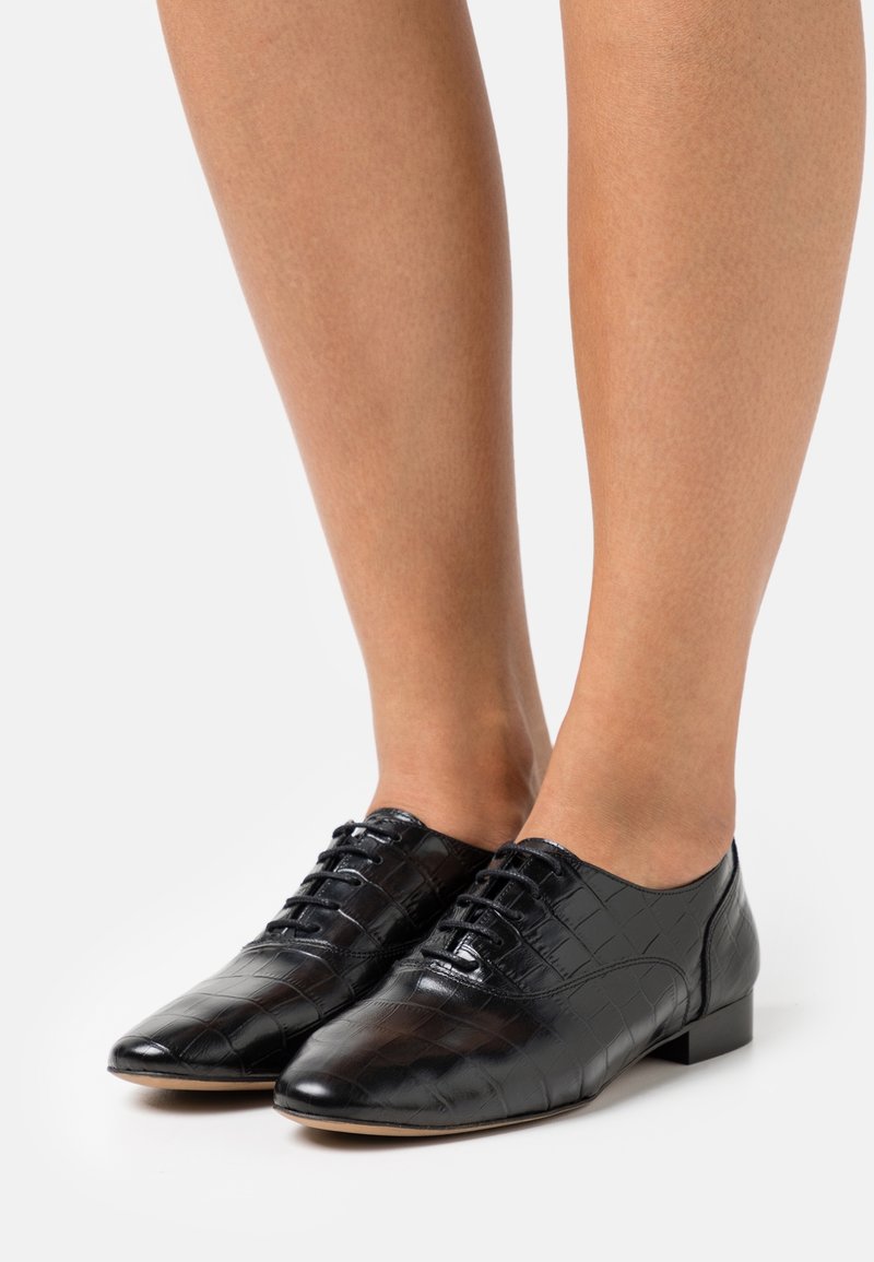 Chaussures en cuir noir avec un motif crocodile, dotées d'un petit talon et d'un laçage sur le devant. Texture lisse et design à bout pointu.