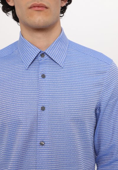 Camisa de botón azul claro con un patrón repetitivo de texto blanco, cierre de botones y un diseño de cuello clásico. Textura de tela suave.
