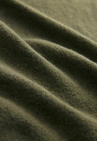 Material verde închis, cu o suprafață moale și texturată, având cute ondulate care pun în evidență țesătura sa netedă și uniformă.