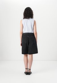 Black denim shorts with a loose fit, featuring back pockets and a zipper fly, paired with a light blue sleeveless top.
