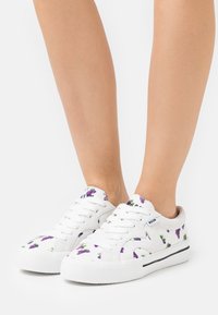 Weiße Leinensneaker mit lila Traubenblumenmuster, runder Zehenpartie, Schnürsenkeln und einer weißen Gummisohle mit einem schwarzen Streifen.
