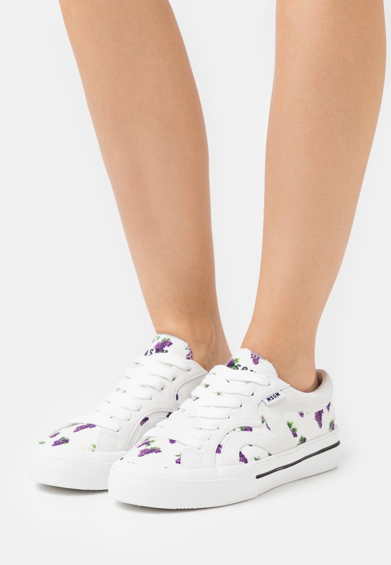 Weiße Leinensneaker mit lila Traubenblumenmuster, runder Zehenpartie, Schnürsenkeln und einer weißen Gummisohle mit einem schwarzen Streifen.