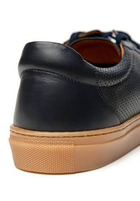 Granatowe skórzane trampki z perforowanym wzorem, brązowym wnętrzem oraz teksturowaną gumową podeszwą z gładkim obcasem.