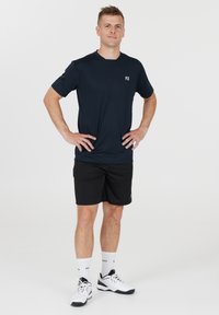 Marinblå träningströja med korta ärmar, i kombination med svarta shorts. Vit logga på bröstet, bärs med vita strumpor och svarta träningsskor.