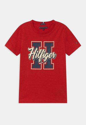 Czerwona bawełniana koszulka z krótkim rękawem, z dużą granatową literą "H" i kremowym napisem "Hilfiger" na piersi, logo Tommy Hilfiger na rękawie.