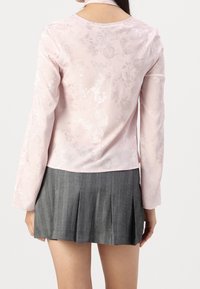 Maglietta a maniche lunghe di un rosa chiaro con motivi floreali; tessuto testurizzato. Abbinata a una gonna grigia plissettata con linee verticali.