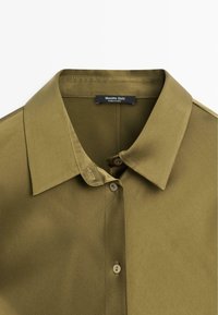 Camicia verde oliva con colletto classico, chiusura a bottoni e texture liscia. L'etichetta riporta 'Massimo Dutti'. Presenta un delicato dettaglio di cucitura.