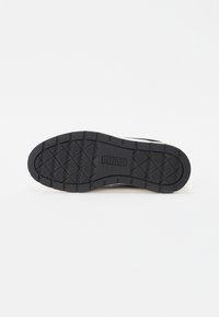 Black rubber shoe sole with textured grip, featuring a geometric pattern and embossed brand logo. Flat and wide design for stability.