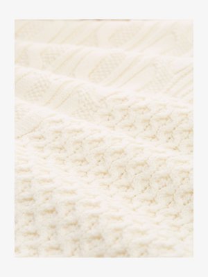 Kremowy, dziergany koc z teksturowanymi wzorami, w tym warkoczami i wypukłymi ściegami, prezentujący różnorodne sploty i grubości.