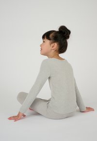 Maglietta grigia chiara a maniche lunghe e leggings coordinati, realizzati in un materiale morbido, mostrati su un bambino seduto di profilo, con un semplice scollo rotondo.