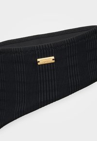 Black ribbed fabric headband featuring a small gold metal logo plate with "COPENHAGEN STUDIOS." Textured surface, elastic design for fit.