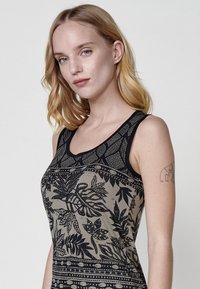 Top débardeur noir et taupe avec un motif de feuilles, encolure dégagée et bretelles noires contrastantes. Texture douce, coupe ajustée et détails graphiques.