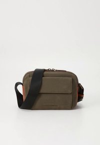 Τσάντα ώμου από καμβά σε ελαιίσιο πράσινο με καφέ λεπτομέρειες, ορθογώνιο σχήμα, μπροστινή τσέπη, κλείσιμο με φερμουάρ και ρυθμιζόμενο μαύρο λουρί.