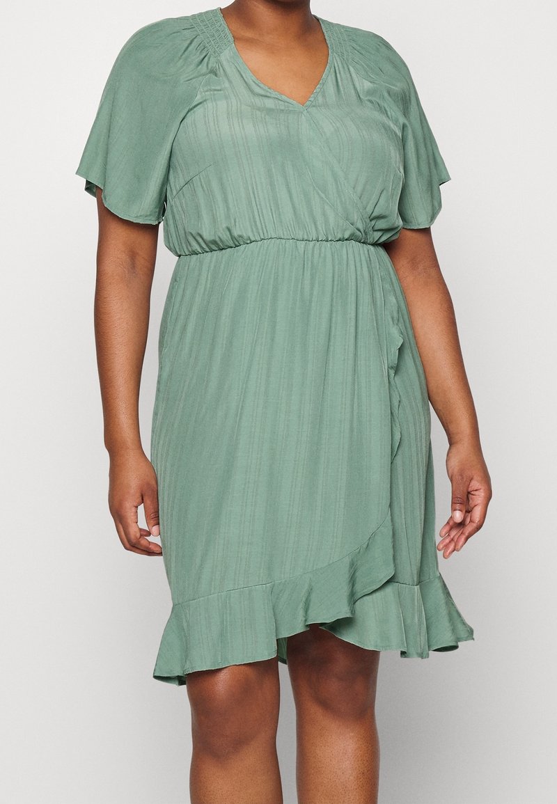 Robe verte mi-longue avec manches courtes évasées, encolure en V, corsage froncé et ourlet volanté ; fabriquée à partir d'un tissu texturé.