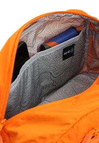 Innenraum eines orangefarbenen Rucksacks mit einem gemusterten grauen Futter, mehreren Fächern und einer RFID-abschirmenden Tasche. Die Formen umfassen rechteckige und runde.