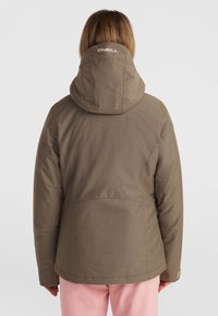 Olijfgroene geïsoleerde jas met een capuchon, met een gestructureerde stof, logo op de achterkant en een effen ontwerp. Ggedragen met roze broek.