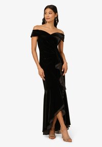 Zwart fluwelen off-shoulder jurk met een getailleerde silhouette, rimpelrand en een hoge split tot boven de dij. Verfraaid met delicate bandjes.