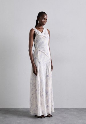 Maxikjole i lysecrème stof med blomsterblå mønstre. Har en cowl-halsudskæring, slim fit og en flydende nederdel. Kombineret med sorte sandaler.