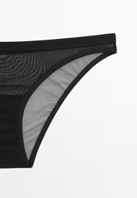Zwarte onderbroek met een mesh ontwerp, voorzien van een soepele elastische tailleband en een contrasterend doorschijnend paneel aan de zijkant.