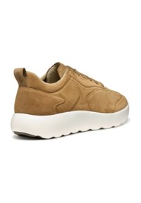 Baskets en suede marron clair avec une épaisse semelle blanche, présentant des bords arrondis et une languette au talon pour un enfilage facile.