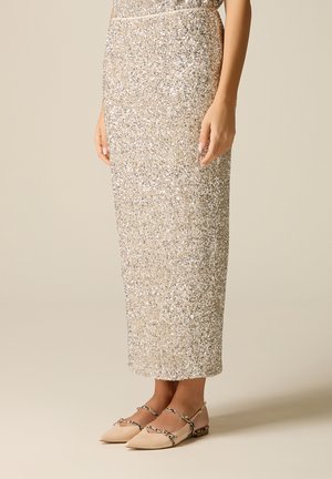 Schimmernder silberner Midirock mit Pailletten, kombiniert mit beigen spitzen Ballerinas mit dünnen gekreuzten Riemchen und niedrigem Absatz.