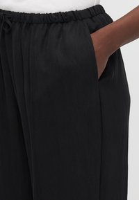 Mustat, kevyet housut joustavalla vyöhön, sivutaskuilla ja pehmeällä tekstuurilla, sopivat arkikäyttöön.